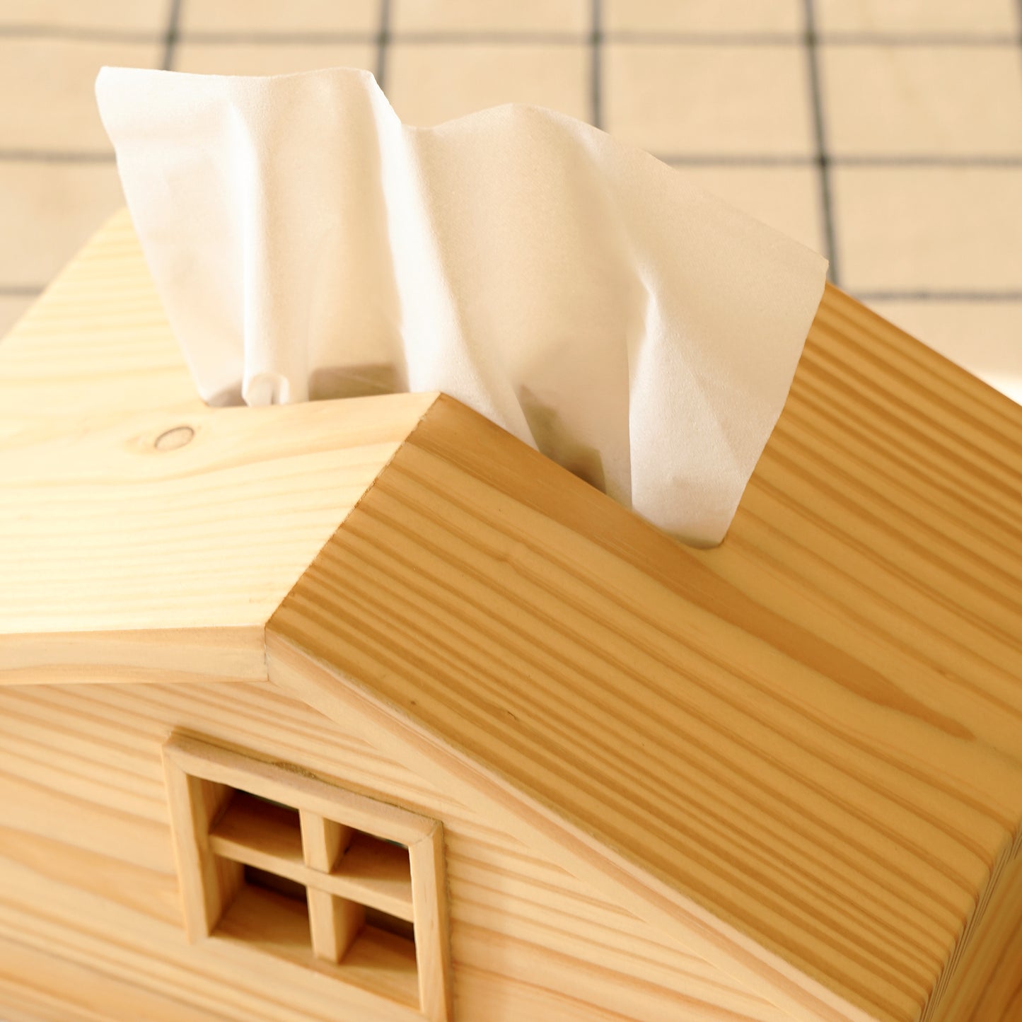 Cabin style tissue holder made of natural wood with a window detail and tissues dispensing from the roof