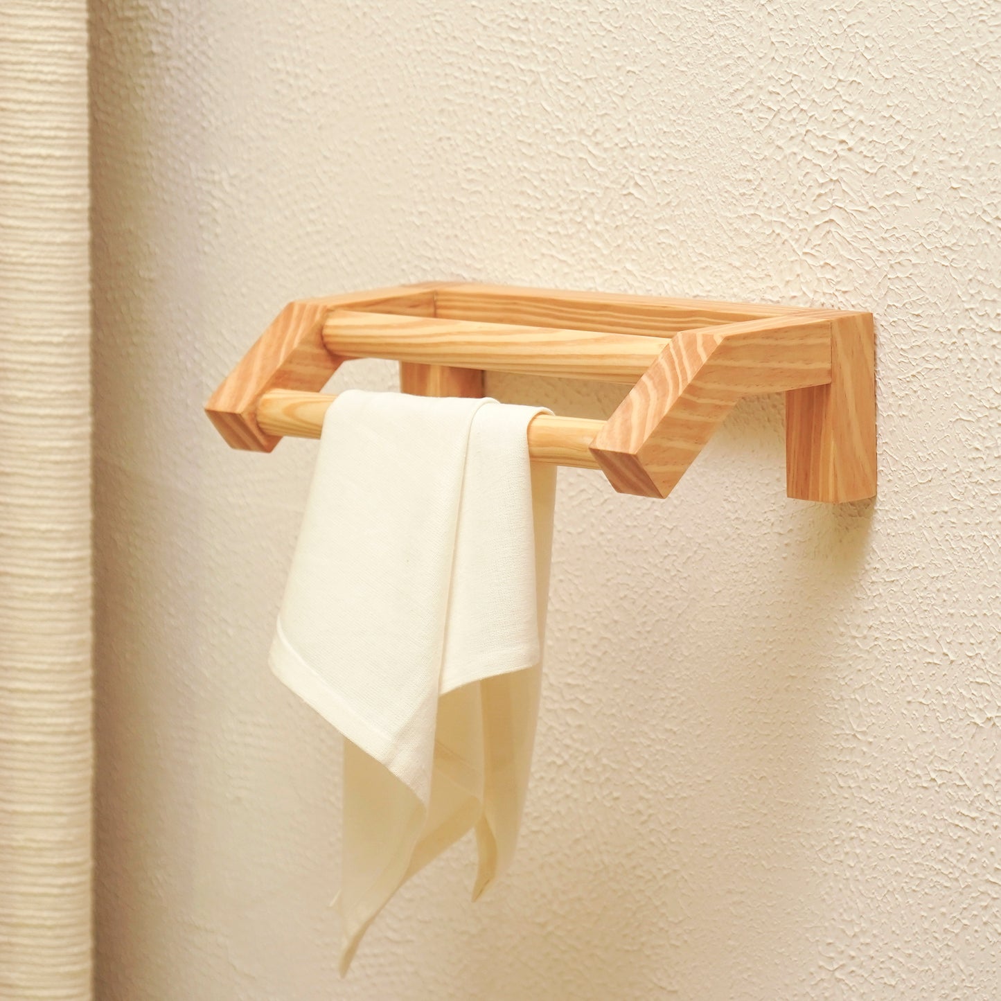 Minimalist wooden hand towel rail mounted on wall with a white towel hanging from it
