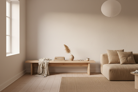 A warm minimalist interior with light matte pinewood furniture, a folded linen throw, a ceramic vase and a stack of books in soft natural light