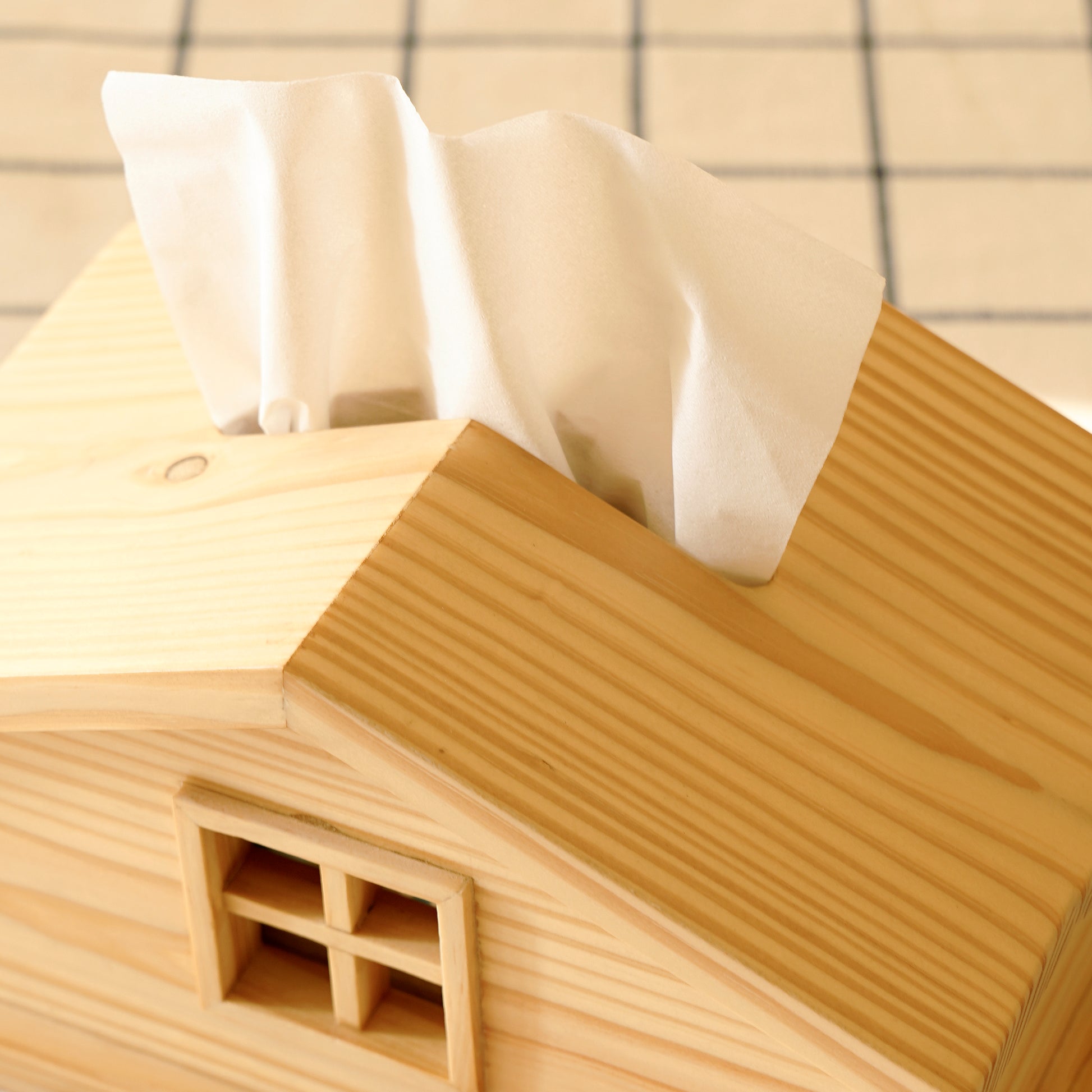 Cabin style tissue holder made of natural wood with a window detail and tissues dispensing from the roof