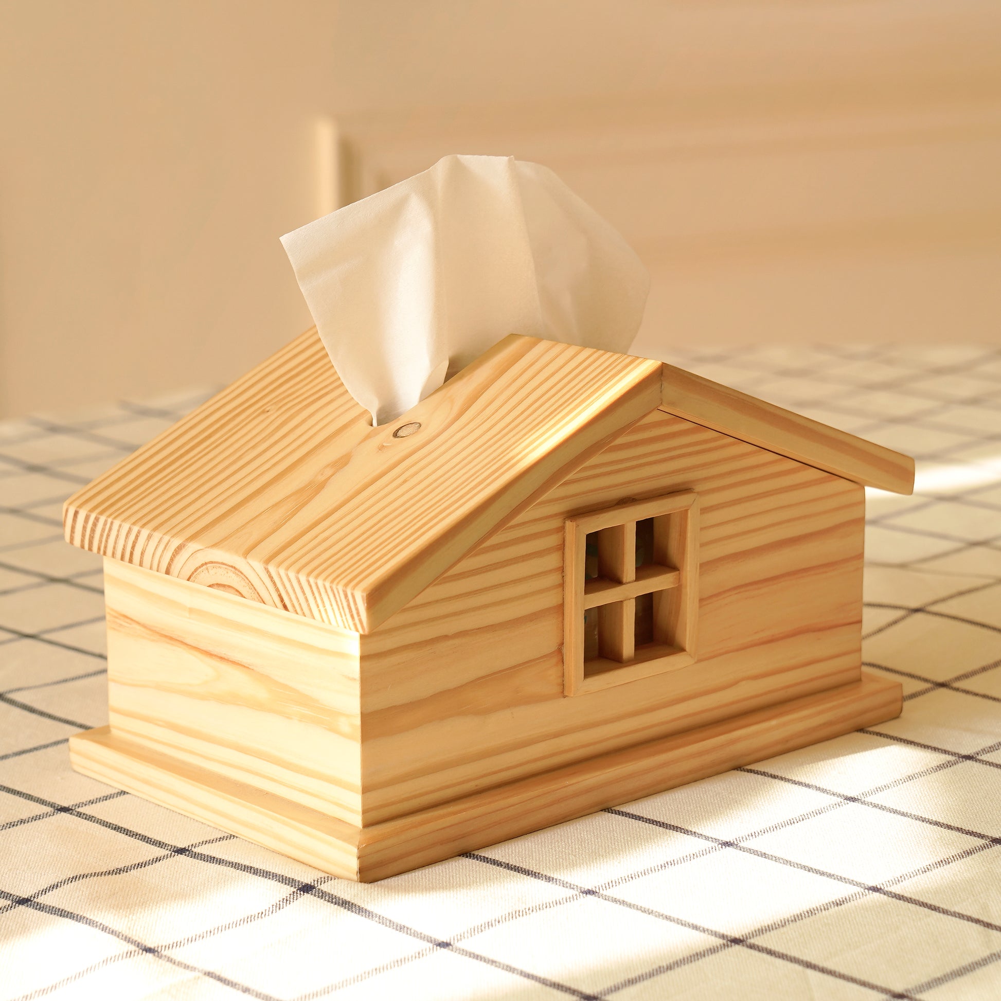 A Good Life cabin style tissue holder made of natural wood shaped like a small house on a checkered tablecloth