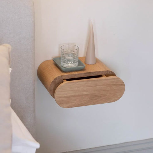 A Good Life minimalist floating bedside table in light wood with a glass of water and a decorative vase