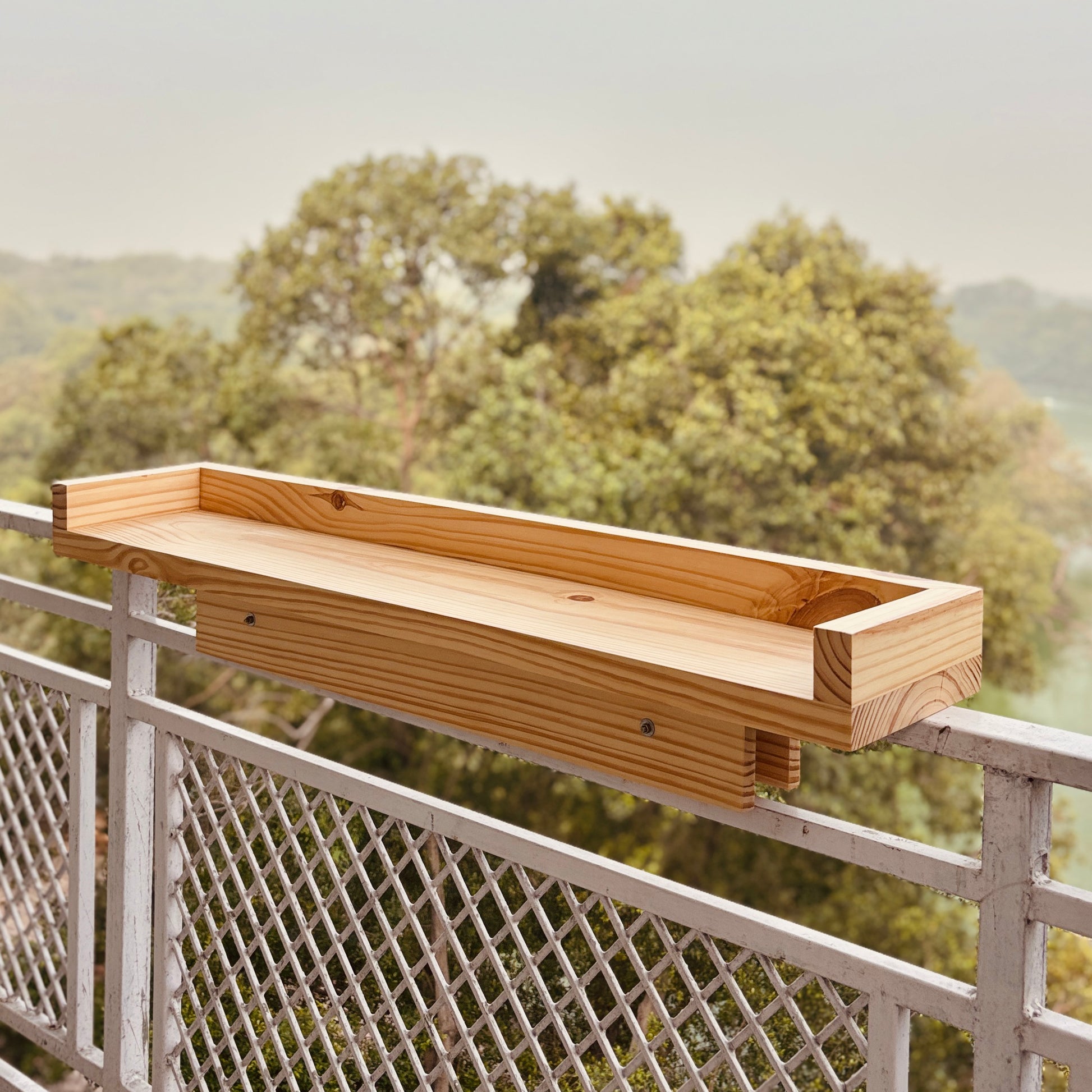 A Good Life pine wood balcony shelf mounted on a metal railing with a forest background