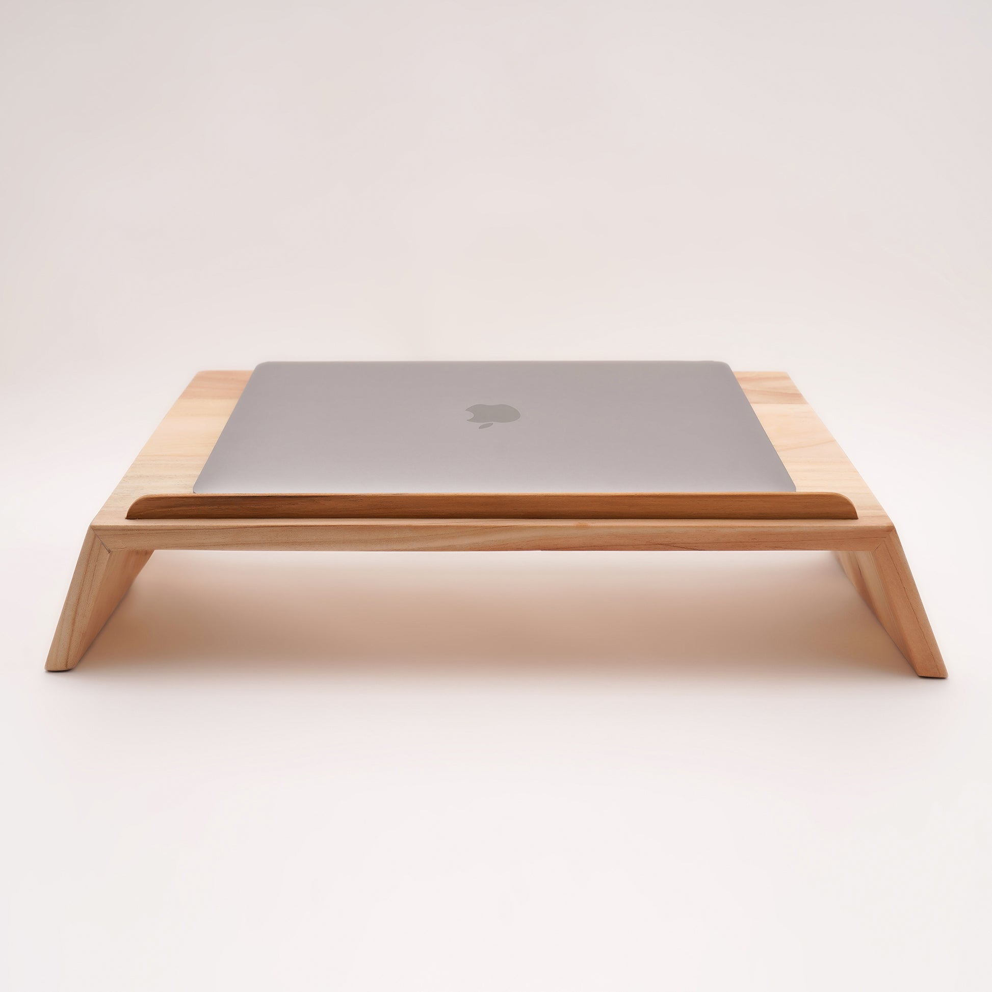 A Good Life pinewood ergonomic work desk laptop stand with a sleek wooden design holding a closed silver laptop

