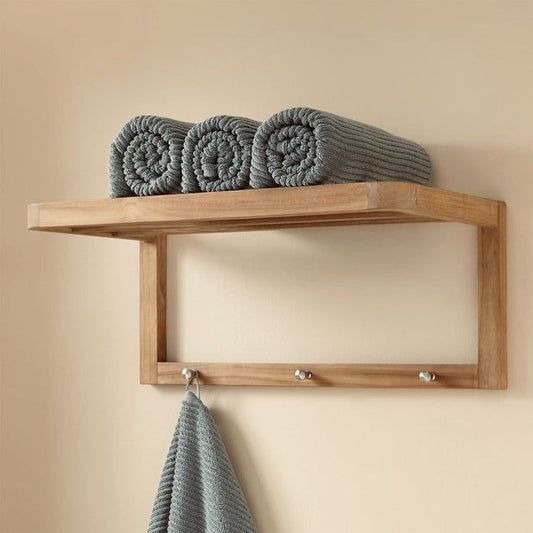 Solid wood towel shelf with hooks holding rolled and hanging gray towels on a beige wall
