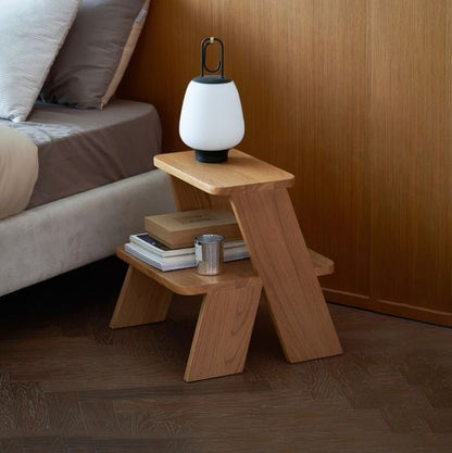 A Good Life wabi-sabi step side table in natural wood next to a bed with a modern lamp on top