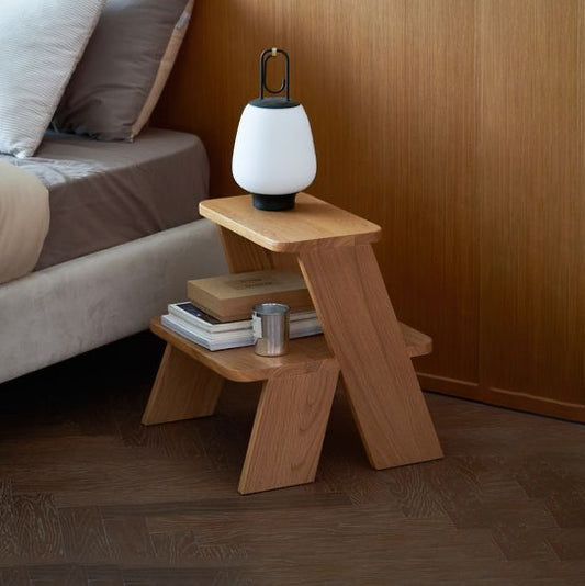 A Good Life wabi-sabi step side table in natural wood next to a bed with a modern lamp on top