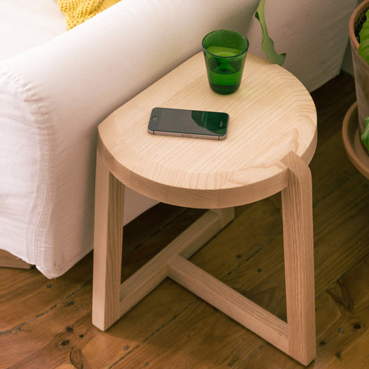 A Good Life minimalist wooden nesting tables side table with a green glass and smartphone on top beside a white sofa